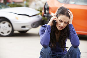 worried woman sitting on the sidewalk and talking on the phone after an accident
